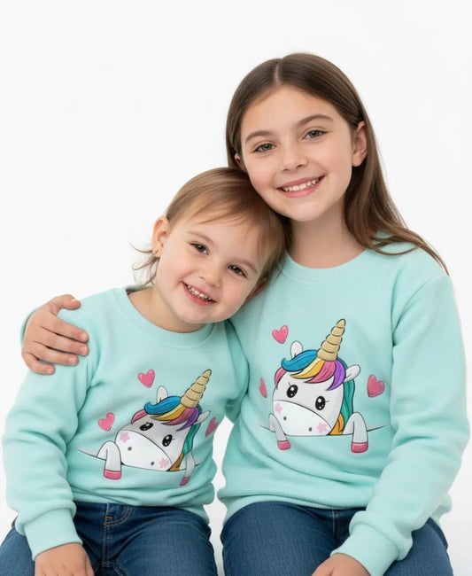 Two children wearing light blue sweaters with unicorn designs on a white background