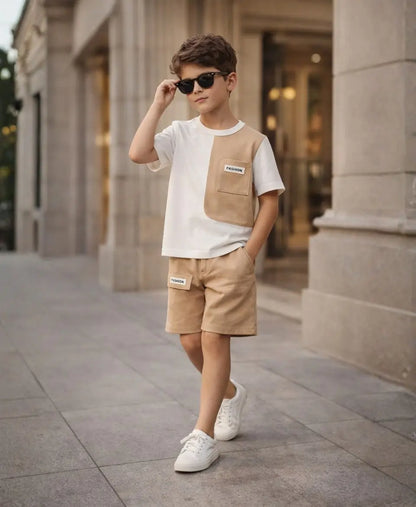 Child wearing a beige and white outfit with sunglasses in front of a building.