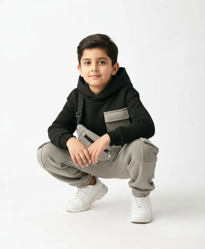 Child wearing a black hoodie and gray overalls on a white background