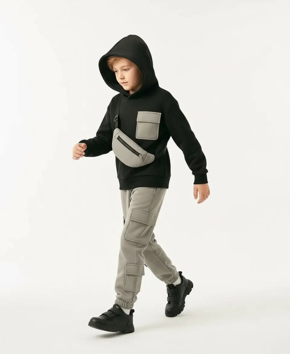Child wearing a black hoodie with a gray front pocket and gray cargo pants on a white background