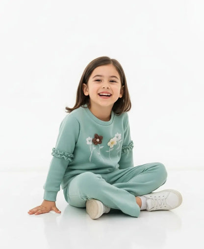 Child wearing a light green outfit with floral designs on a white background