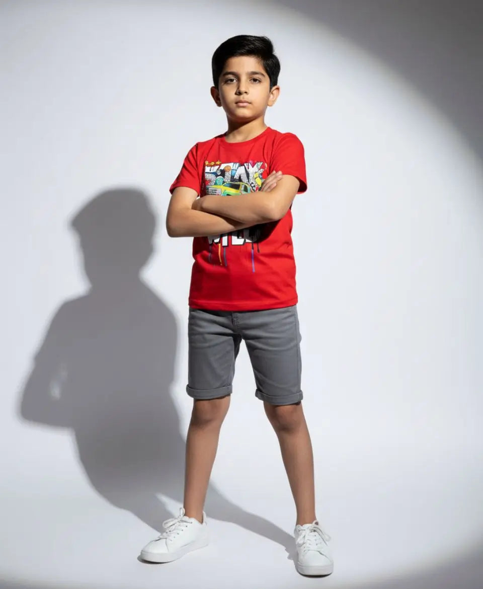 Child wearing a red t-shirt and gray shorts standing against a white background