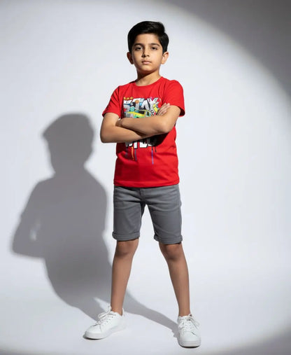 Child wearing a red t-shirt and gray shorts standing against a white background