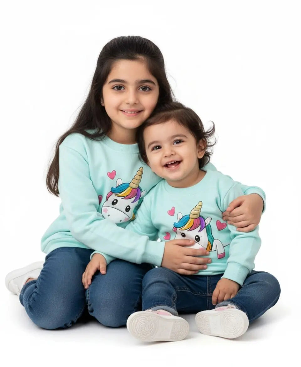 Two children wearing matching light blue sweatshirts with unicorn designs on a white background