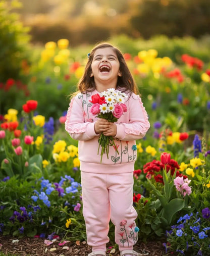Child in a pink outfit holding flowers in a field of colorful flowers