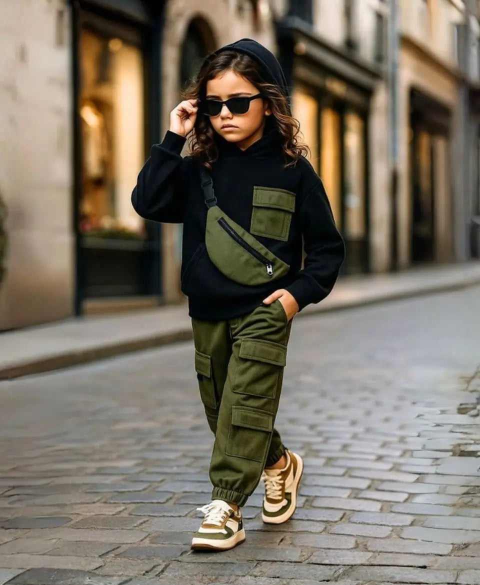 Happy Kidi Child wearing a black hoodie, green cargo pants, and sunglasses on a city street.