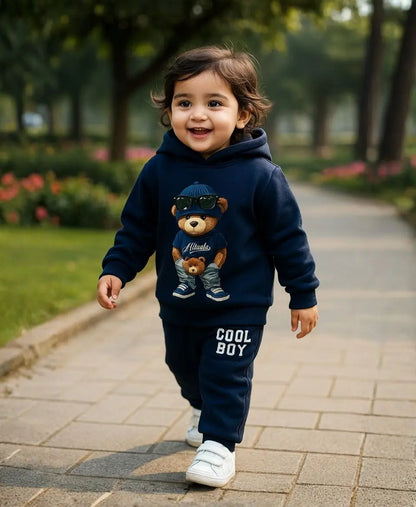 Happy Kidi Child wearing a navy blue hoodie with a teddy bear graphic and 'Cool Boy' text, walking on a path outdoors.