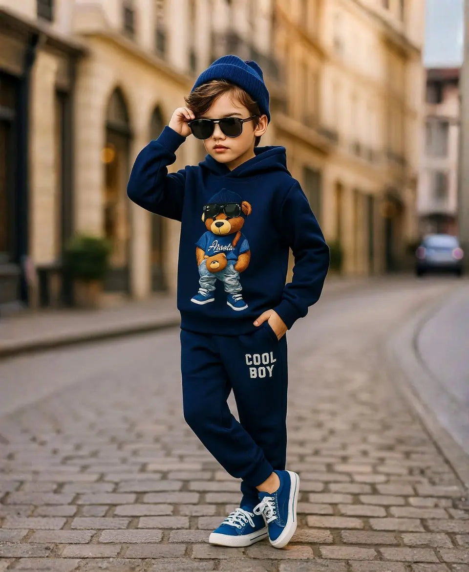 Happy Kidi Child wearing a navy blue outfit with a teddy bear graphic and 'Cool Boy' text, standing on a street.
