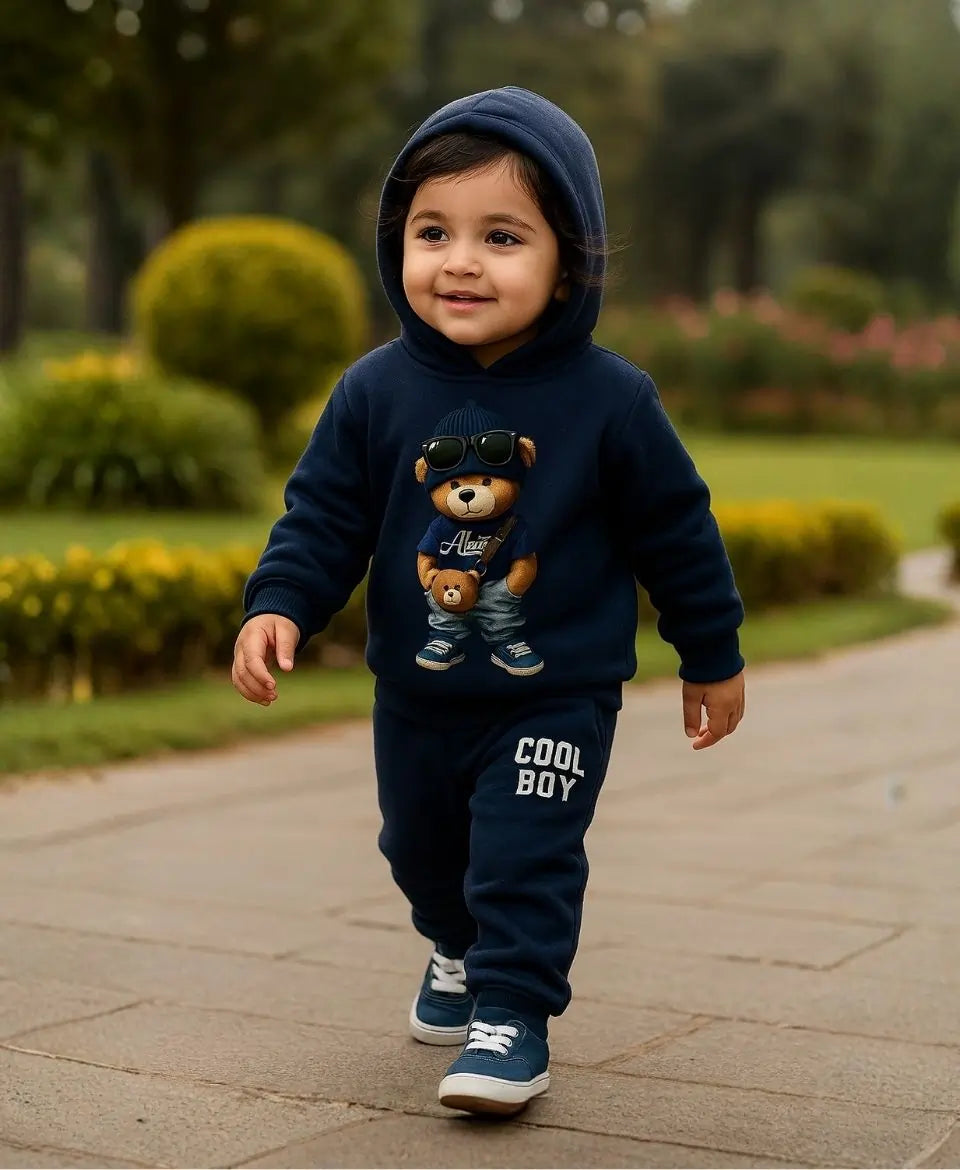 Happy Kidi Child wearing a navy hoodie with a teddy bear design and 'Cool Boy' pants, walking outdoors.