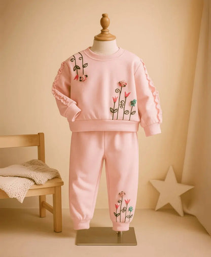 Pink children's outfit with floral designs on a mannequin against a beige background.