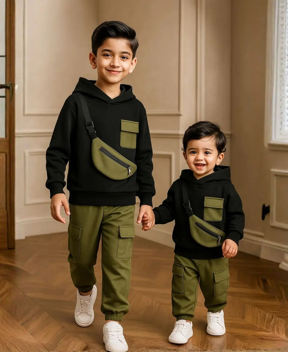 Happy Kidi Two children wearing matching black hoodies and green pants, holding hands indoors.