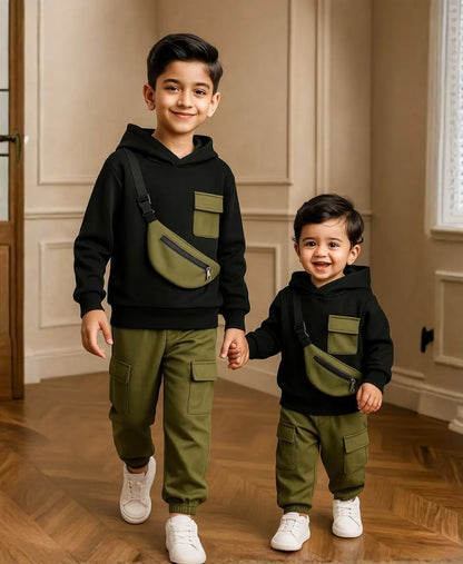 Happy Kidi Two children wearing matching black hoodies and green pants, holding hands indoors.