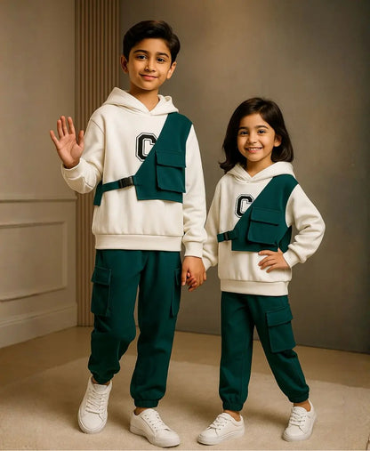 Two children wearing matching outfits with white hoodies and green pants, standing against a neutral background.