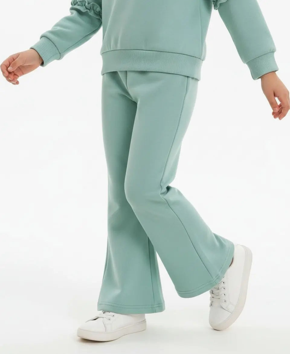 Person wearing a light green tracksuit with white sneakers on a white background