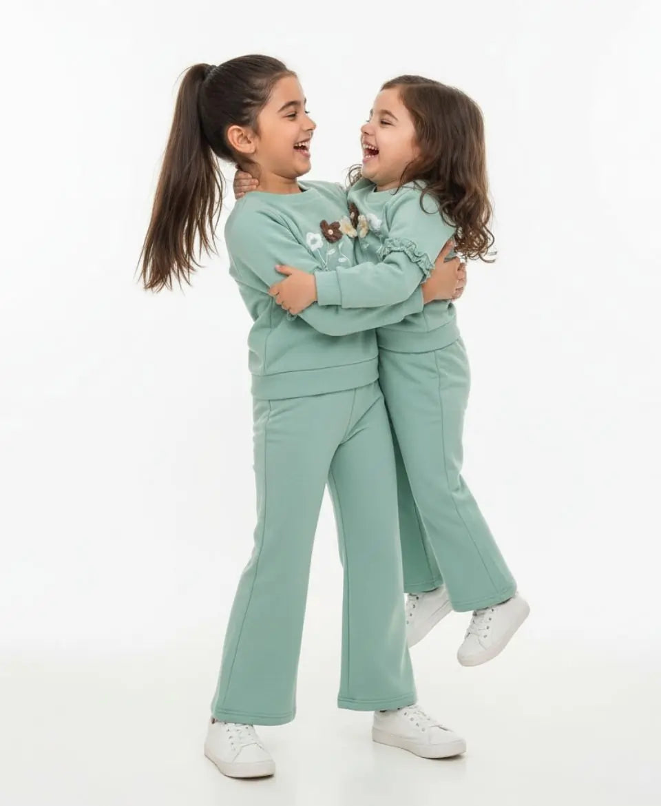 Two children in matching green outfits hugging on a white background