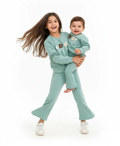 Two children in matching teal outfits on a white background