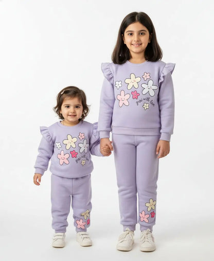 Two children wearing matching lavender outfits with floral designs on a white background