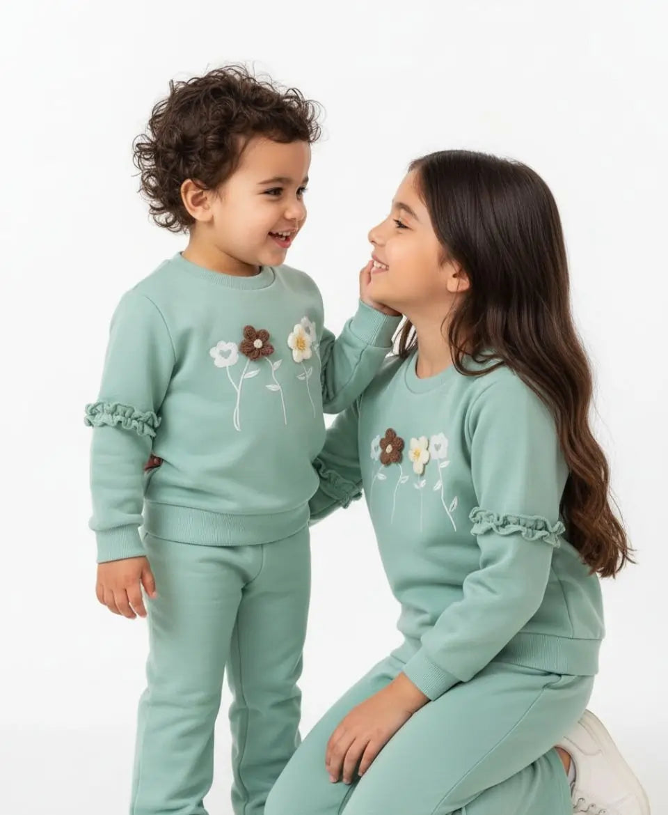 Two children wearing matching light blue sweatsuits with floral designs on a white background