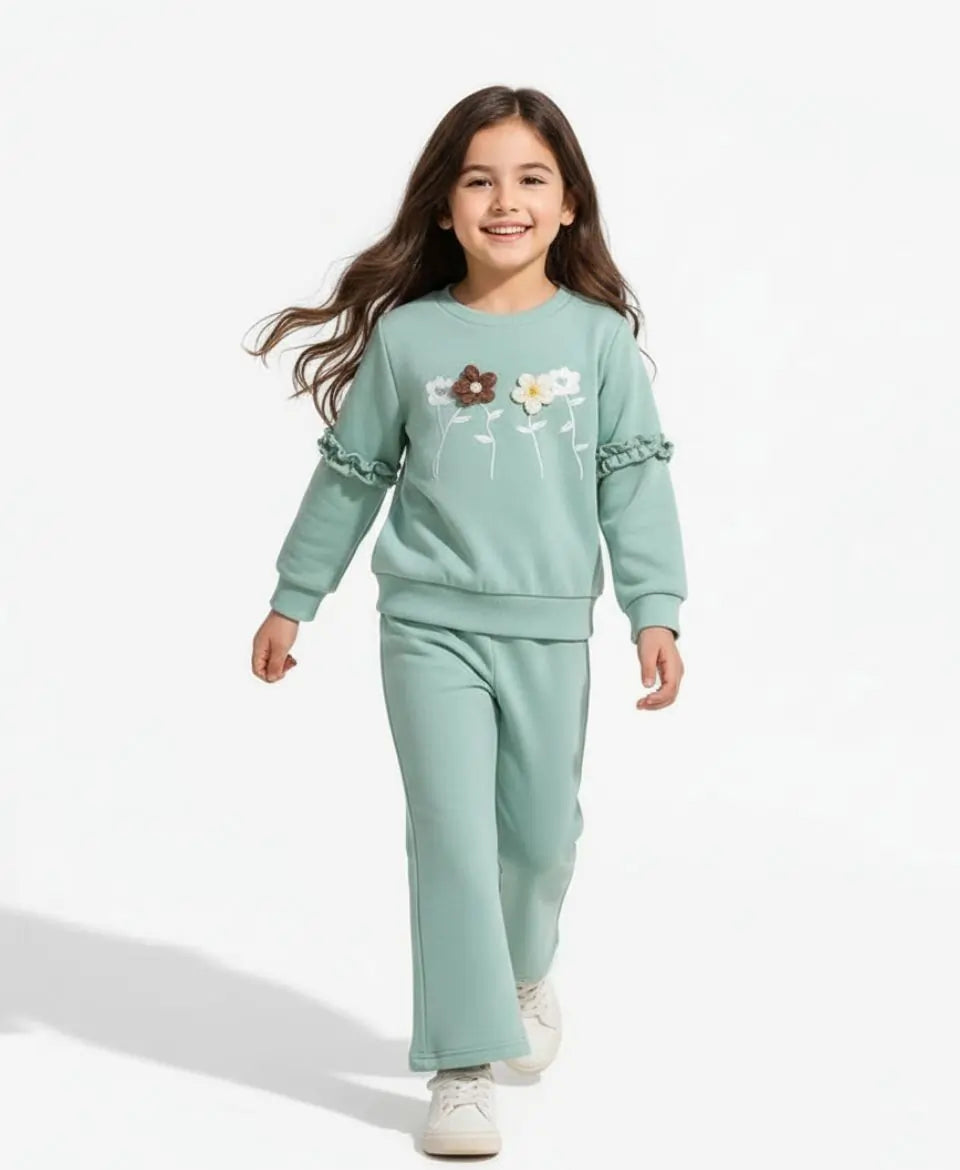 Young girl wearing a light green sweatshirt and pants set with floral designs on a white background