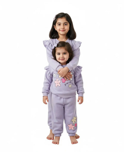 Two children wearing matching lavender outfits with floral designs on a white background
